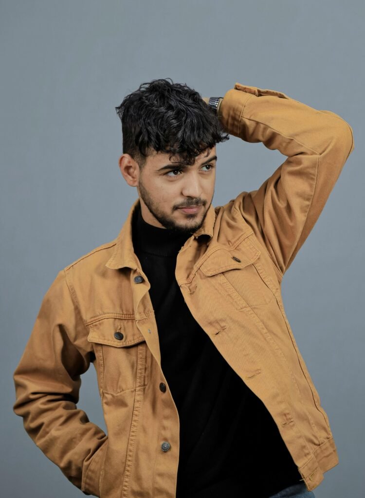 Stylish male model posing in a yellow jacket with a confident look against a gray background.