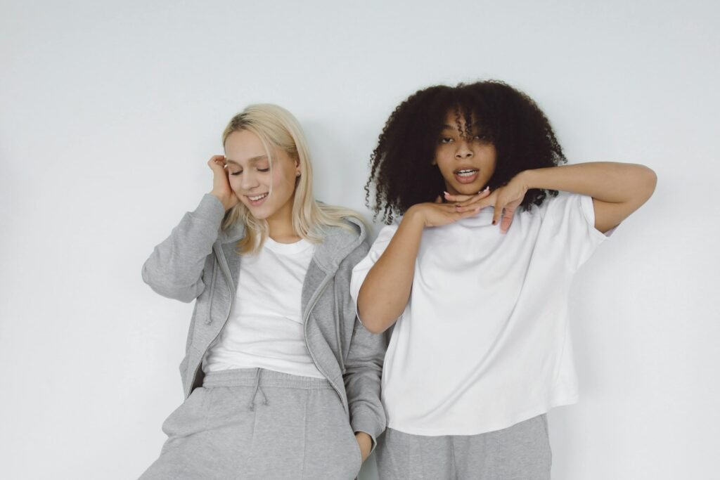Two women in casual wear smiling and posing against a white wall.